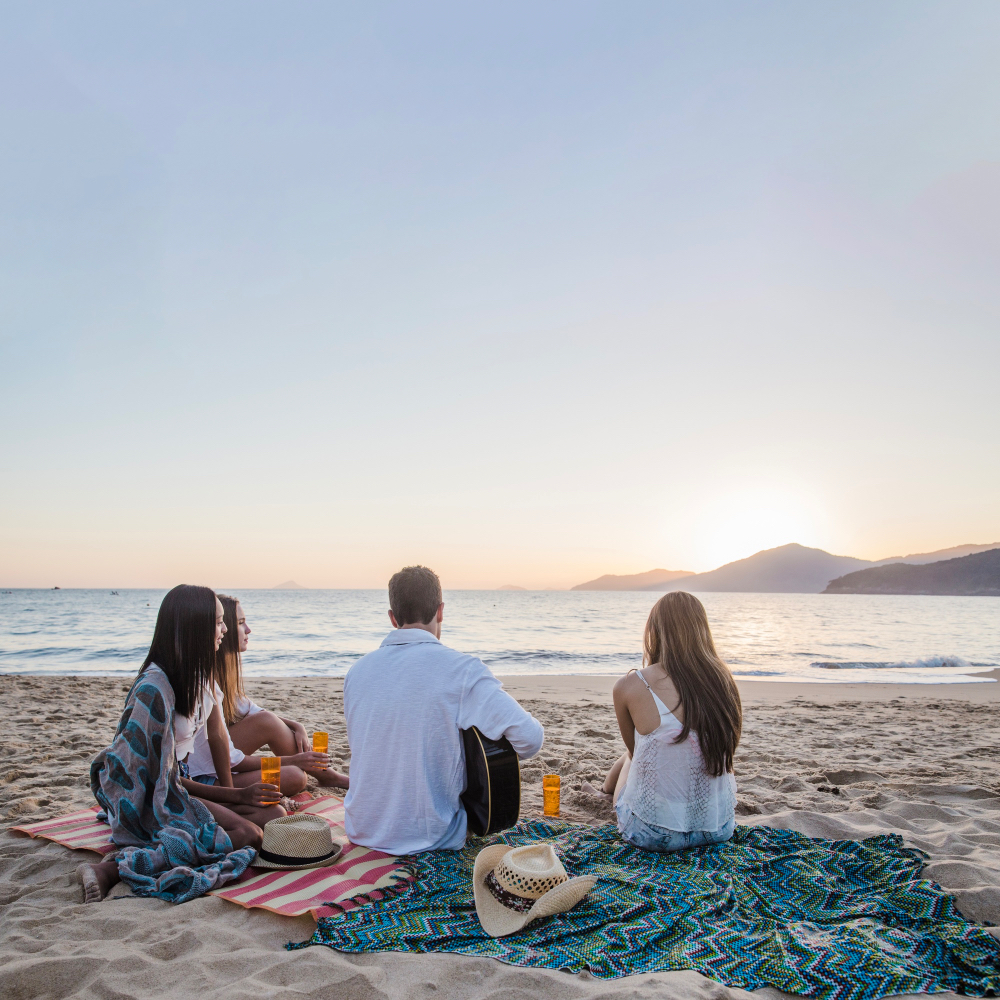 Gruppe sitzt beim Picknick am Strand und genießt den Sonnenuntergang am Atlantik