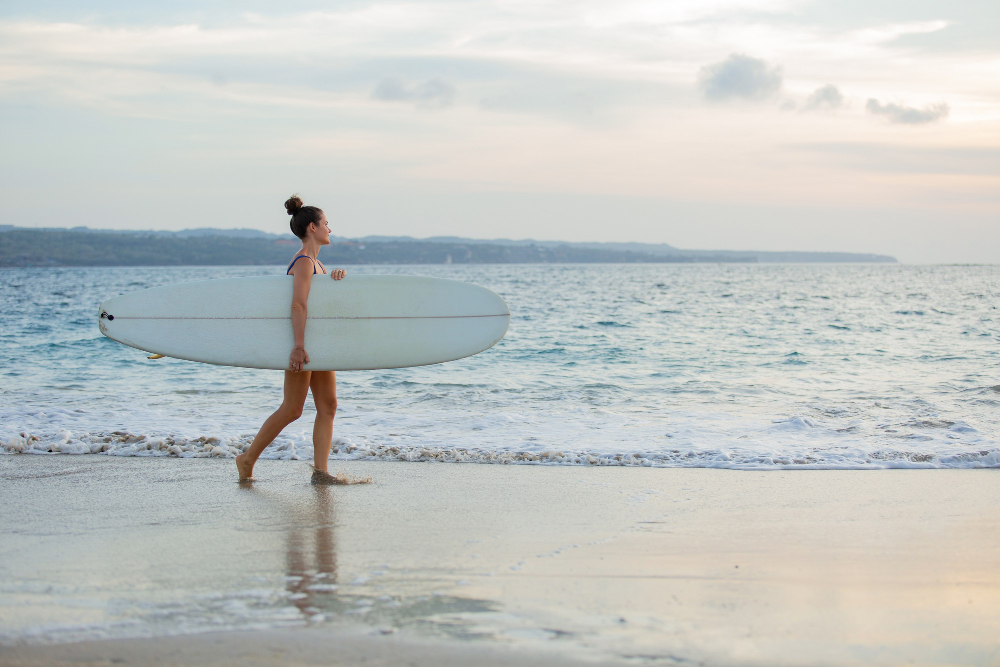 Surferin trägt ihr Longboard am Strand entlang und blickt auf die Wellen des Atlantiks in Frankreich