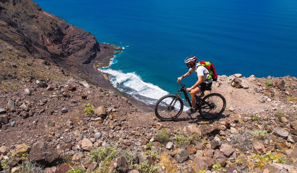 Mountainbiker auf einem felsigen Vulkantrail mit Blick aufs Meer.