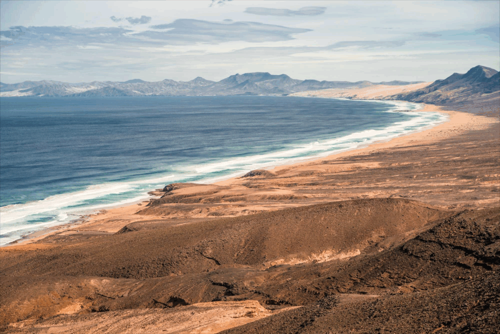 Weitläufige Aussicht auf die Playa de Cofete an der Westküste von Fuerteventura mit endlosem Strand, Atlantikwellen und karger Berglandschaft.