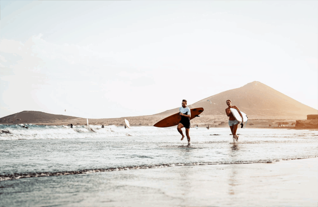 Zwei Surfer laufen mit Boards am Strand von Fuerteventura – Surfurlaub mit Sonne und Meer