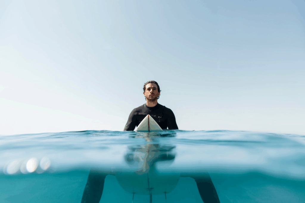 Surfer sitzt im Wasser mit Surfboard – Surftrip in Marokko