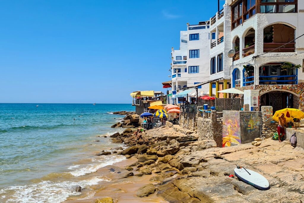 Blick auf Taghazout in Marokko mit Strand, bunten Häusern und Surfbrettern am Meer