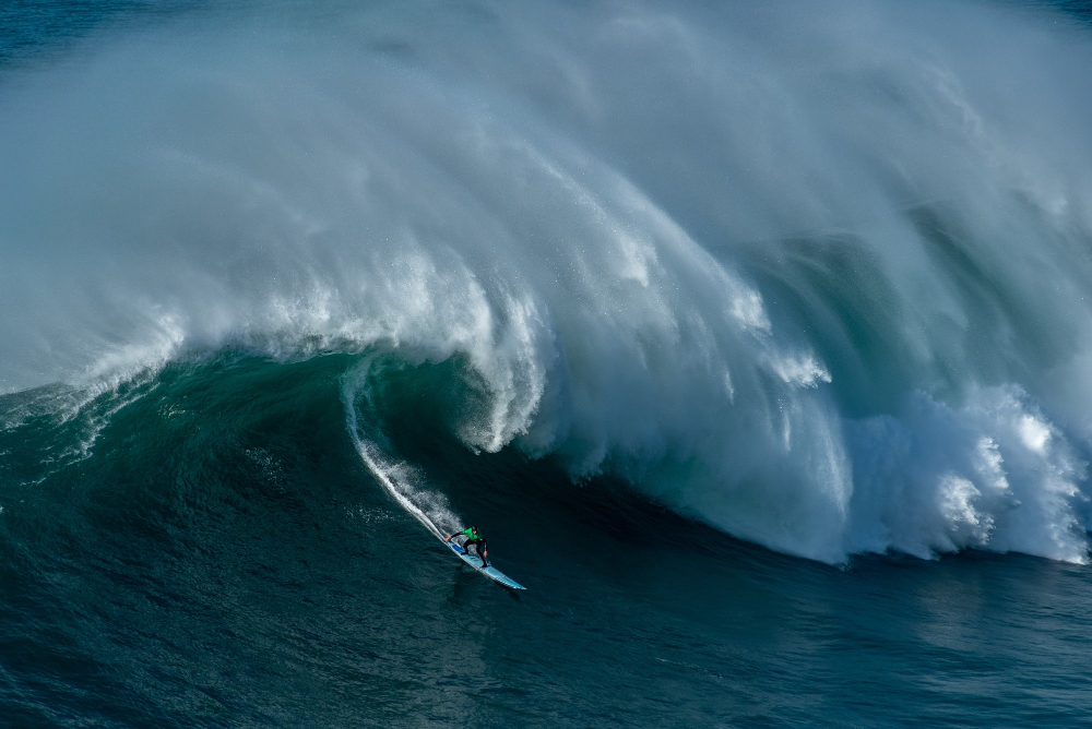 Surfer reitet eine der riesigen Big Waves in Nazaré, Portugal – weltbekanntes Mekka für Big-Wave-Surfen.