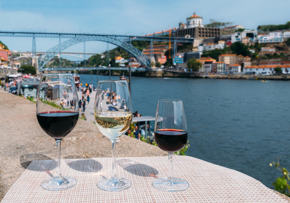 Drei Weingläser mit Portwein am Ufer des Douro vor der Dom Luís I Brücke in Porto – Genuss und Kulinarik in Portugals zweitgrößter Stadt