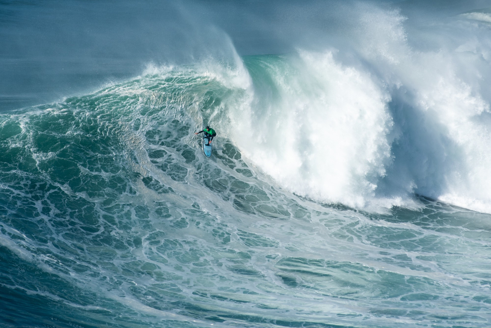 urfer reitet eine Welle vor den beeindruckenden Klippen der Algarve in Portugal
