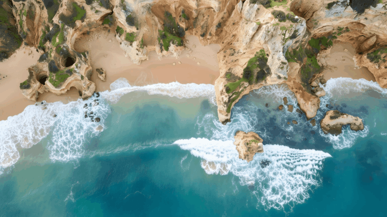 Drohnenaufnahme der Algarve-Küste in Portugal mit goldenen Felsen, Sandstrand und Wellen – perfekte Bedingungen zum Surfen.
