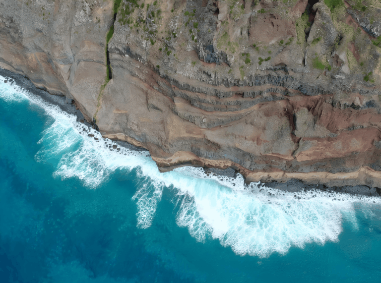 Drohnenaufnahme: Atlantikwellen treffen auf die vulkanische Steilküste mit sichtbaren Lavaschichten an Teneriffas Nordküste.