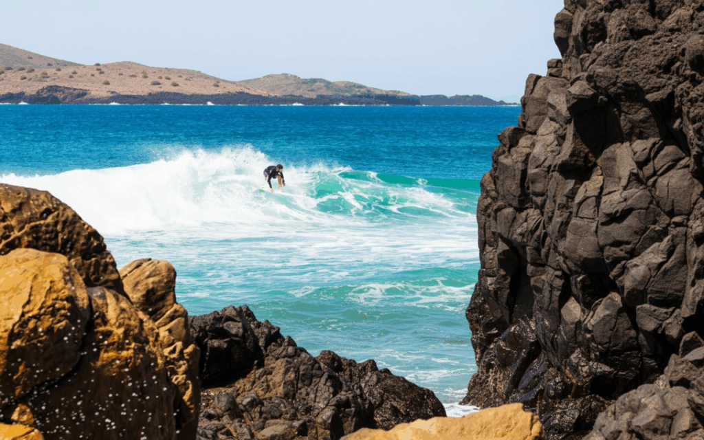 Surfer reitet eine Welle zwischen dunklen Lavaklippen an der Nordküste Teneriffas – Natur, Action und Atlantikenergie.