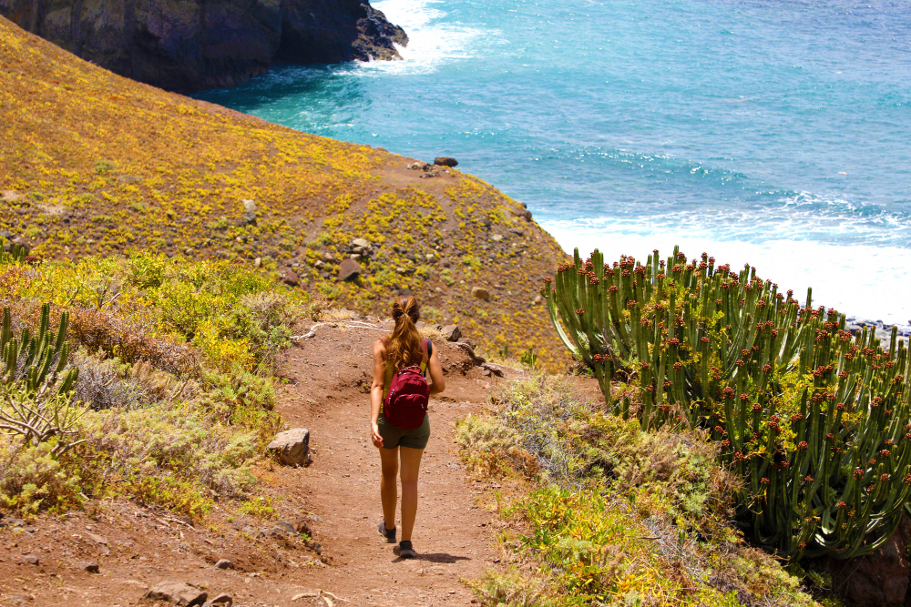 Wanderin auf dem Pfad zur Masca-Schlucht auf Teneriffa mit Blick auf das Meer und die typische kanarische Vegetation.
