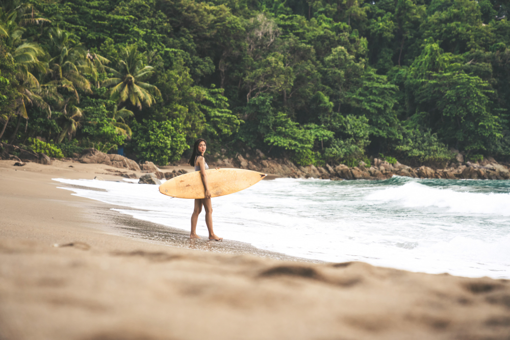Surferin mit Board am tropischen Strand von Sri Lanka, umgeben von dichtem Dschungel und Palmen